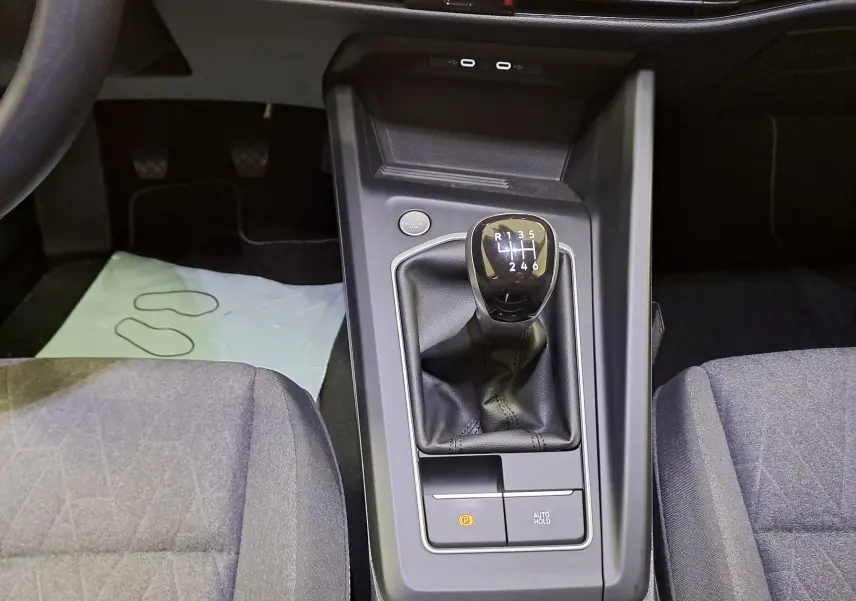 Vue intérieure centrée sur la console centrale d'une Volkswagen Golf 1.5 eTSI avec levier de vitesses manuel et sièges gris.