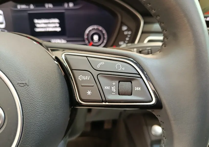 Gros plan sur les commandes multimédias au volant cuir noir d'une Audi A5 gris clair, tableau de bord flou en arrière-plan.