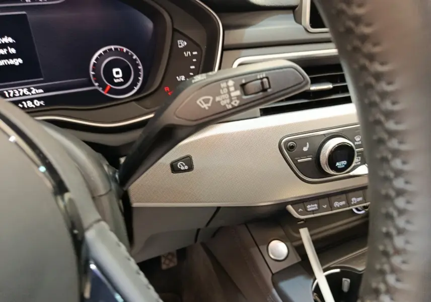 Vue intérieure côté conducteur de l'Audi A5 gris clair, avec tableau de bord digital et commandes de climatisation visibles.