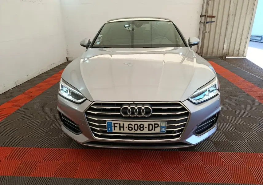 Vue frontale d'une Audi A5 gris clair avec phares LED allumés et calandre chromée dans un garage.