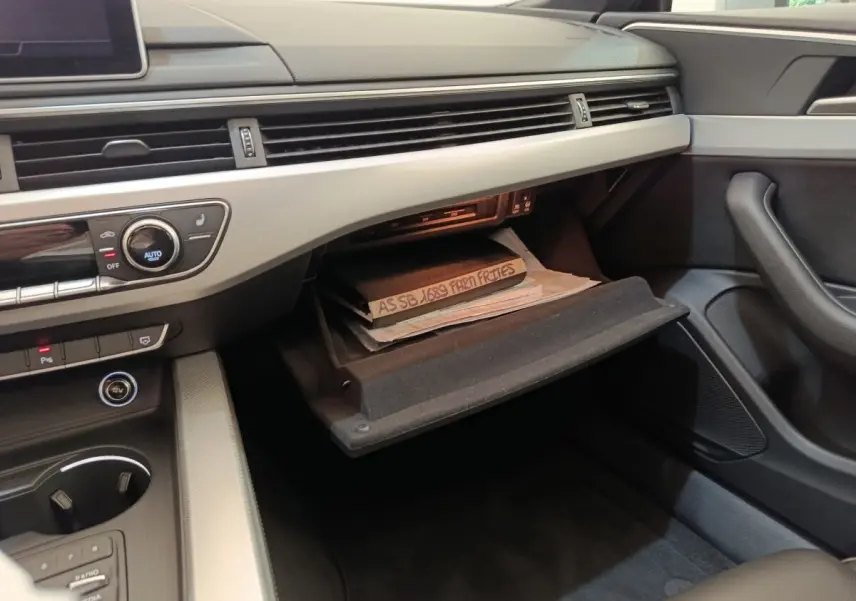 Vue intérieure côté passager de l'Audi A5 2019, boîte à gants ouverte avec documents visibles, tableau de bord gris clair.
