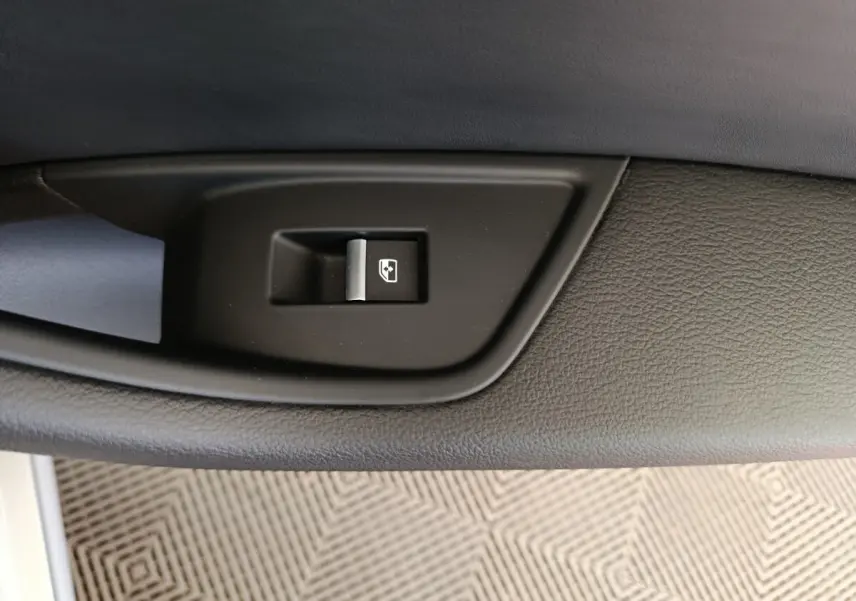 Gros plan sur le bouton de commande de la vitre électrique, sur la porte intérieure noire de l'Audi A5 gris clair.