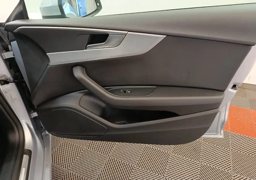 Vue rapprochée de la porte avant gauche de l'Audi A5 gris clair, avec poignée intégrée et commande de vitre.