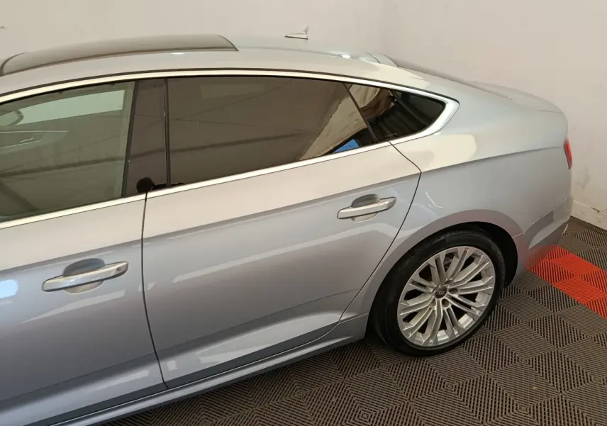 Vue côté droit arrière d'une Audi A5 gris clair avec jante alliage et vitres teintées dans un intérieur fermé.
