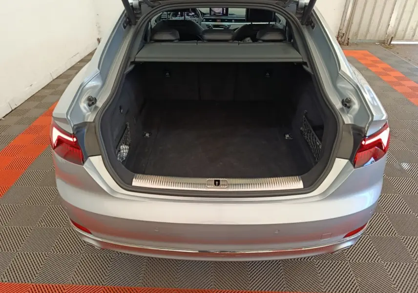 Coffre ouvert vu de l'arrière d'une Audi A5 gris clair, montrant un espace de chargement spacieux et propre.