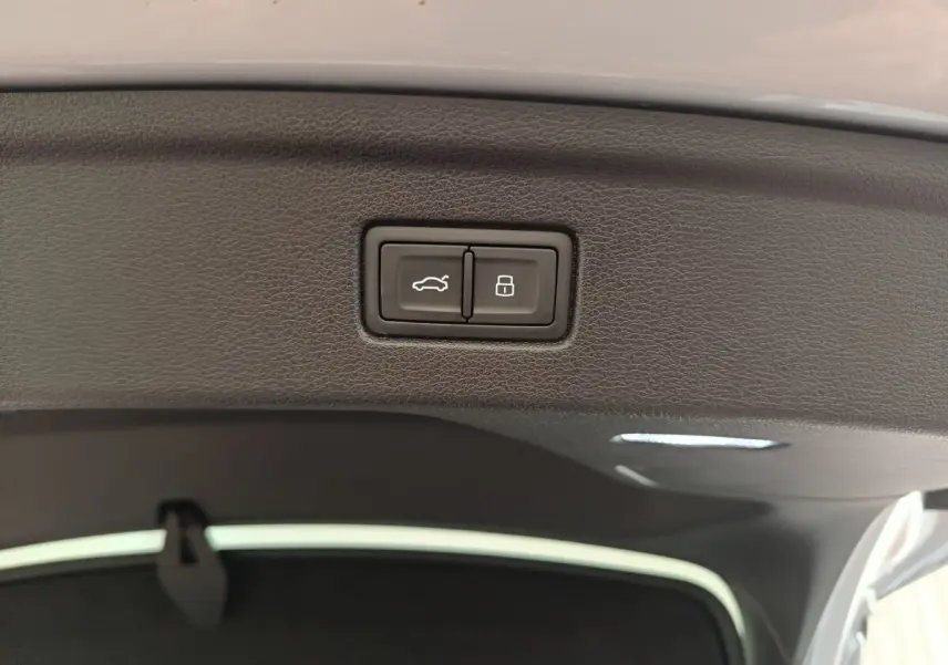 Boutons d'ouverture et de verrouillage du coffre sur la garniture intérieure du hayon d'un Audi A5 gris clair.