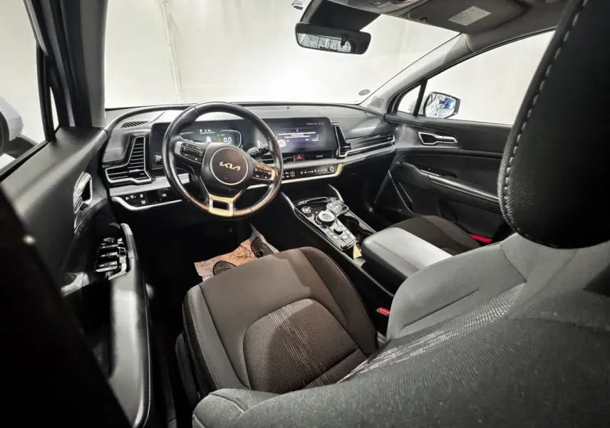 Vue intérieure avant droite du Kia Sportage 2024, tableau de bord noir avec écran tactile et volant cuir multifonctions.
