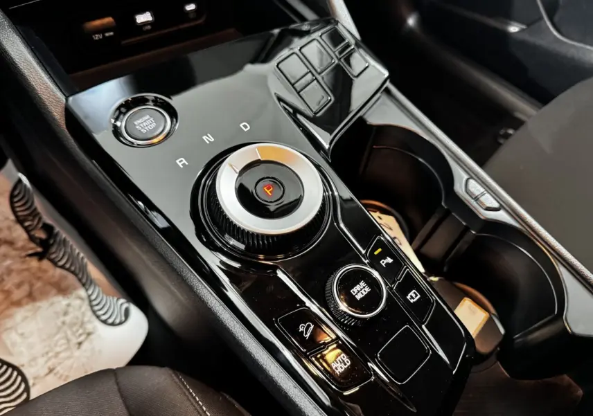 Gros plan sur la console centrale noire brillante du Kia Sportage 2024, avec molette de sélection de vitesse et bouton start/stop.