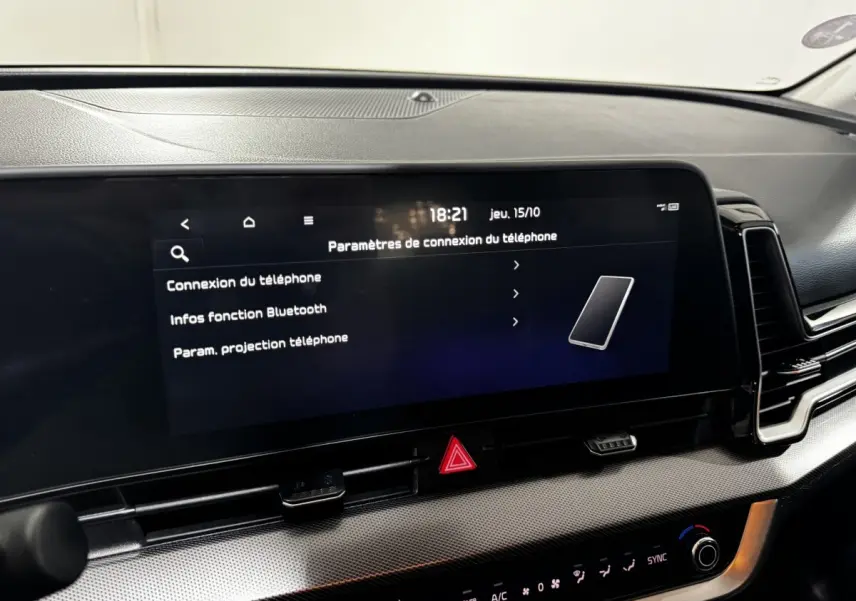 Gros plan sur l'écran tactile central du tableau de bord du Kia Sportage blanc 2024 affichant les paramètres de connexion téléphone.
