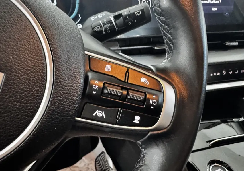 Gros plan sur le volant cuir noir de la KIA SPORTAGE 2024 avec commandes multifonctions et tableau de bord digital.