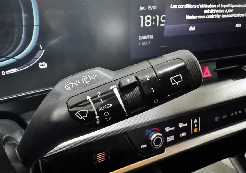 Gros plan sur la commande des essuie-glaces du tableau de bord numérique du Kia Sportage blanc 2024, affichage multifonctions visible.