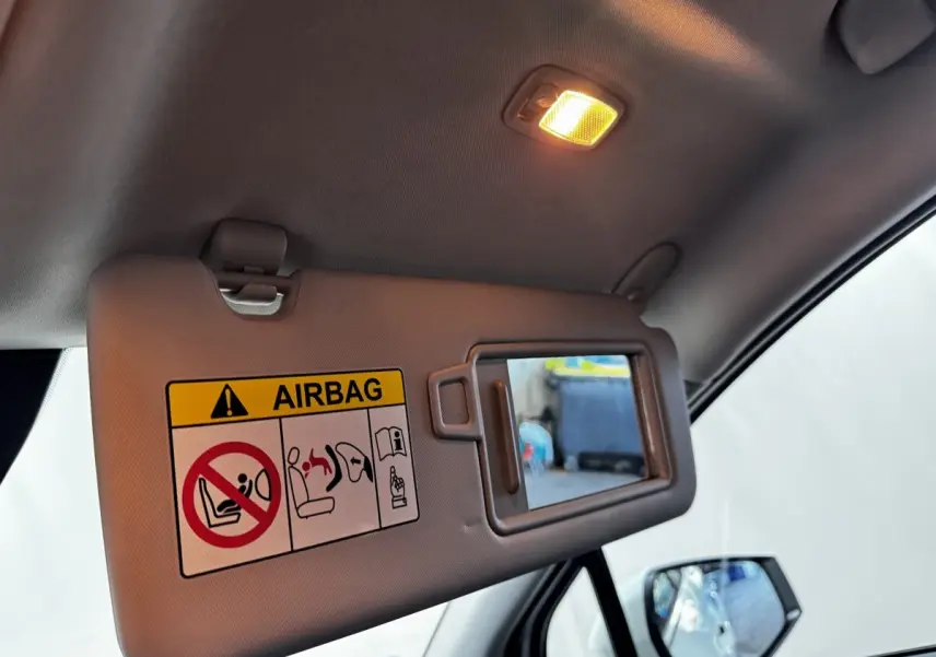 Détail intérieur du pare-soleil côté conducteur avec miroir et avertissement airbag dans un Kia Sportage blanc.