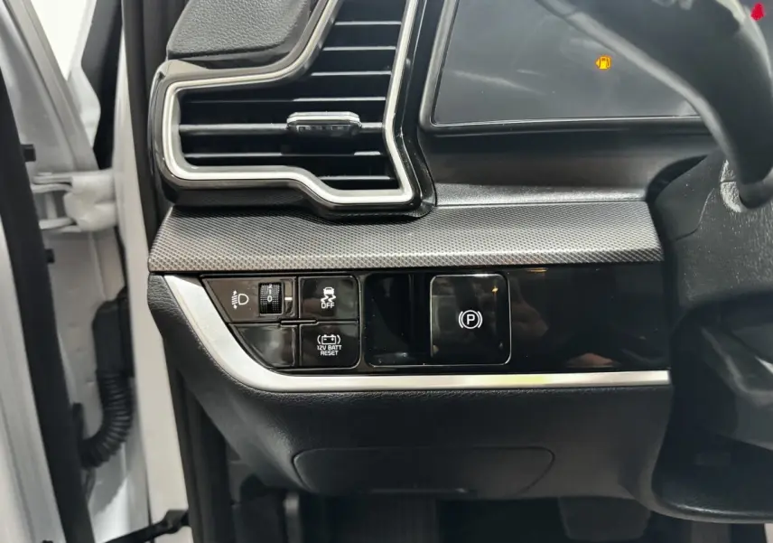 Détail du tableau de bord côté gauche du Kia Sportage blanc 2024 avec commandes d'éclairage et frein à main électrique.
