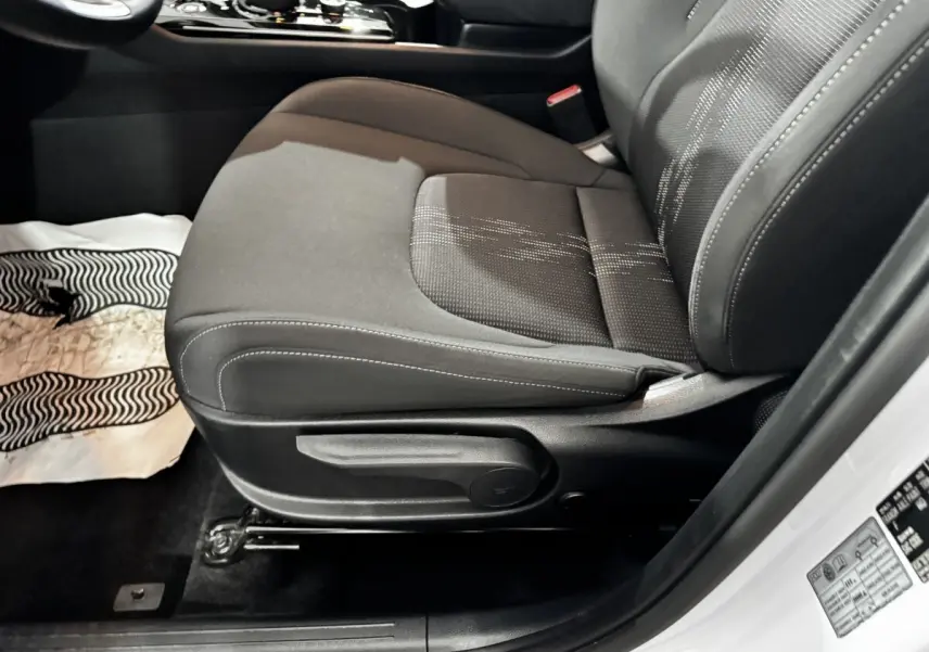 Vue rapprochée du siège avant gauche noir du Kia Sportage blanc 2024, avec réglage manuel visible.