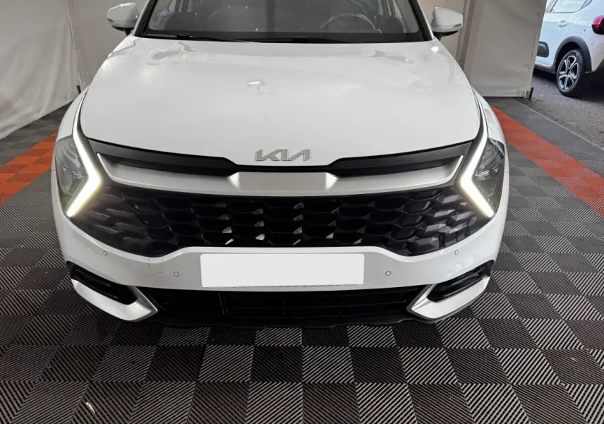 Vue frontale d'un KIA Sportage blanc 2024 avec calandre noire et feux diurnes LED en forme de flèche.