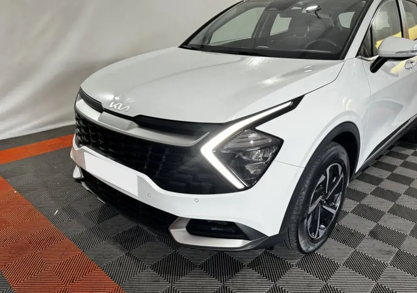 KIA Sportage blanc vu de 3/4 avant droit avec feux LED en forme de flèche et calandre noire distinctive.