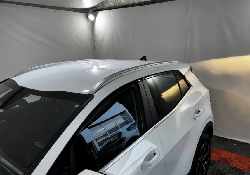 Vue 3/4 arrière droite du KIA SPORTAGE blanc 2024 avec toit et vitres teintées dans un garage fermé.