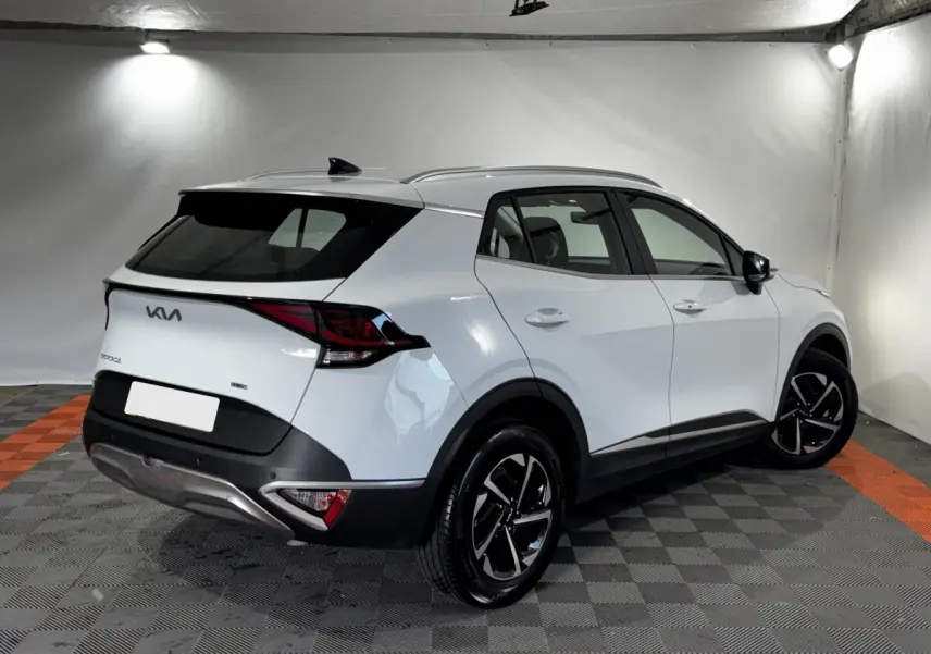 Vue 3/4 arrière droite d'un Kia Sportage blanc 2024 avec jantes noires et toit noir contrasté dans un studio.