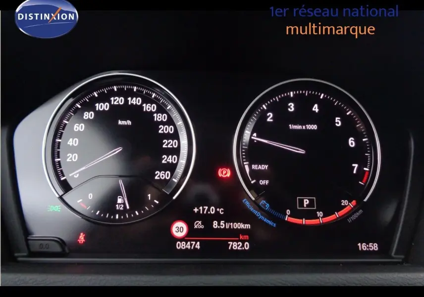 Tableau de bord numérique de BMW X1 blanc Alpine, affichant vitesse, régime moteur et informations de conduite.