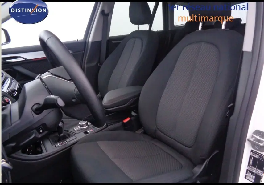 Intérieur du BMW X1 blanc Alpine, vue côté conducteur sur les sièges noirs en tissu et le tableau de bord moderne.