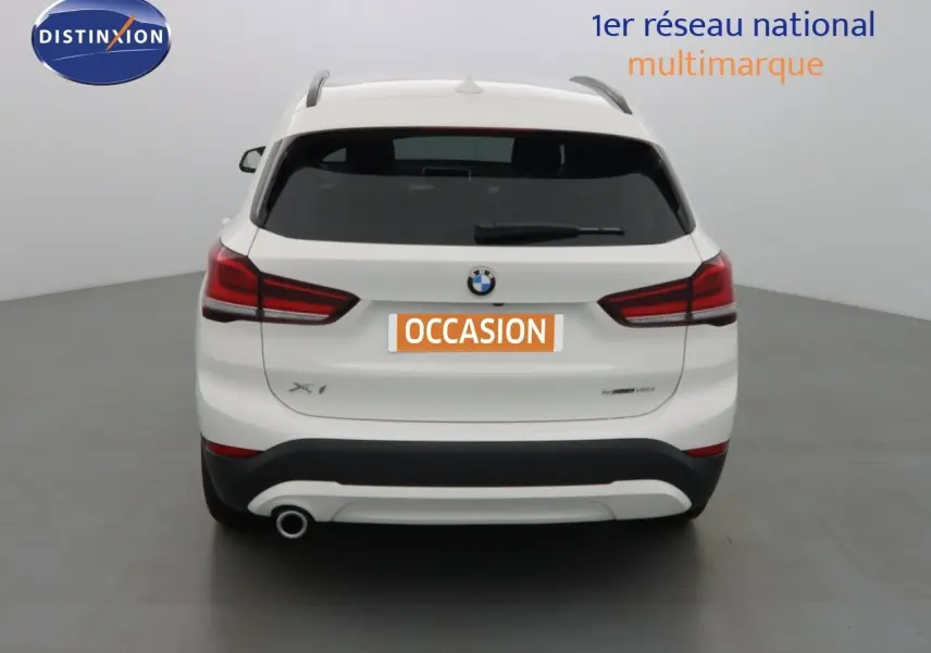 Vue arrière d'un BMW X1 blanc Alpine Metal avec feux rouges et sortie d'échappement unique côté gauche.