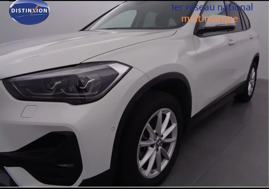 Vue 3/4 avant droit d'un BMW X1 blanc Alpine Metal avec jantes alliage et phares LED distinctifs.