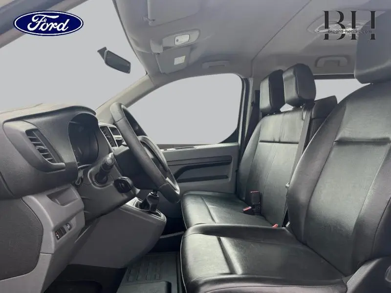 Vue intérieure côté conducteur du Peugeot Expert Fourgon blanc Banquise, montrant les sièges avant en cuir noir et le tableau de bord.