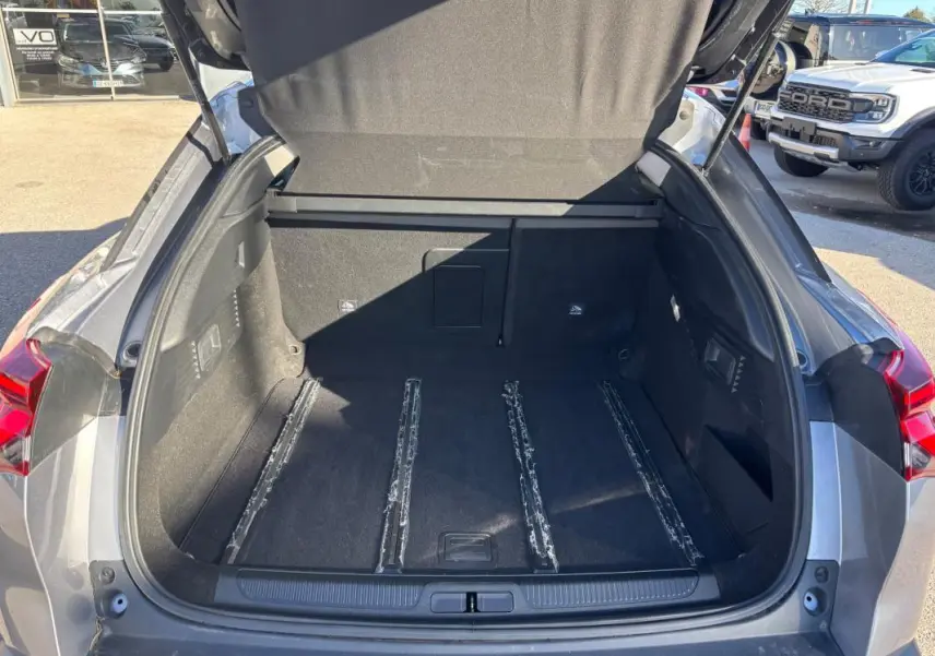 Coffre ouvert vu de l'arrière d'une Citroën C5 X gris foncé, montrant l'espace de chargement vide et les rails au sol.