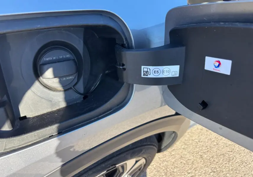 Gros plan sur la trappe à carburant ouverte côté gauche d’une Citroën C5 X gris foncé, avec bouchon essence visible.