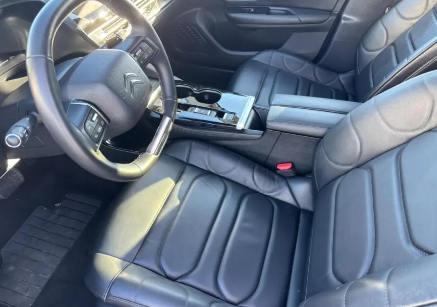 Vue intérieure en plongée du poste de conduite et des sièges en cuir noir du Citroën C5 X 2024 avec accoudoir central et volant cuir.