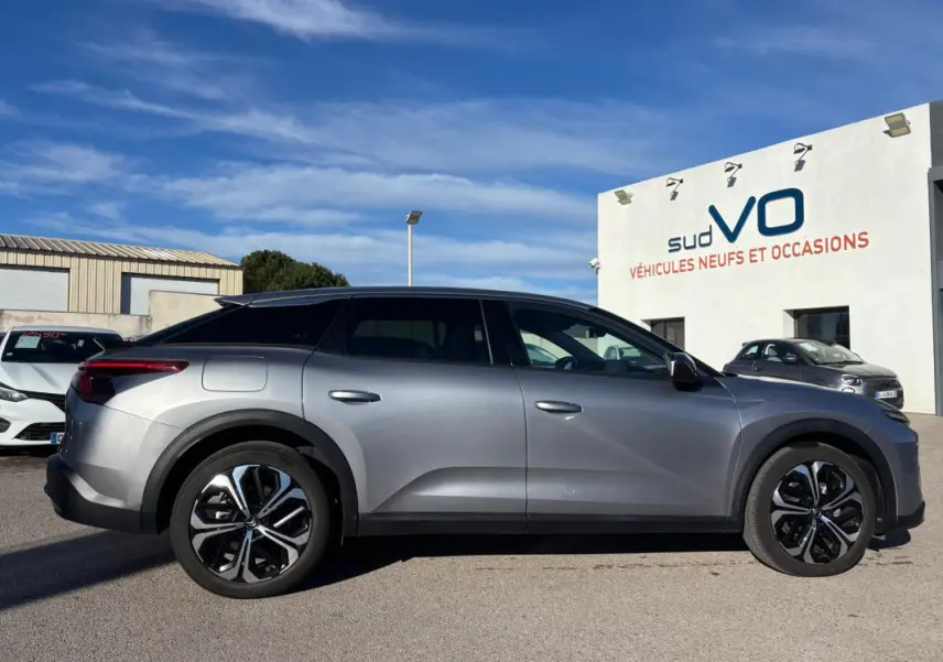 Profil côté gauche du Citroën C5 X gris foncé 2024 avec jantes alliage 19 pouces et barres de toit visibles.