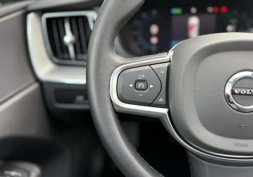 Gros plan sur la partie gauche du volant simili-cuir gris du Volvo XC60 T6 AWD PHEV 2024 avec commandes intégrées.