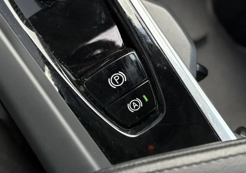 Gros plan sur la console centrale noire brillante du Volvo XC60 2024, montrant les boutons de frein de parking et start/stop.