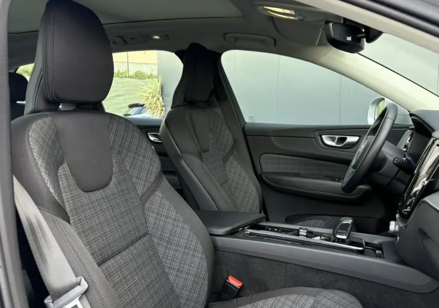 Vue intérieure côté gauche du Volvo XC60 2024, sièges en tissu gris à motif tartan et console centrale noire brillante.