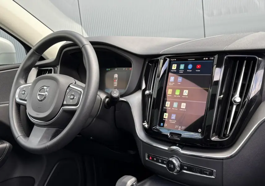 Vue intérieure côté conducteur du Volvo XC60 gris silver 2024, avec volant simili-cuir et écran tactile vertical.