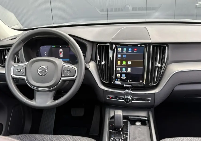 Vue intérieure du tableau de bord du Volvo XC60 gris Silver 2024, avec volant 3 branches et écran tactile vertical.