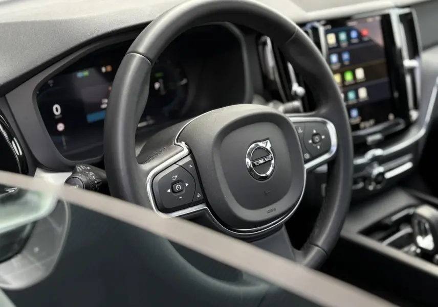 Volant noir 3 branches et tableau de bord digital du Volvo XC60 T6 AWD PHEV 2024, vue intérieure côté conducteur.