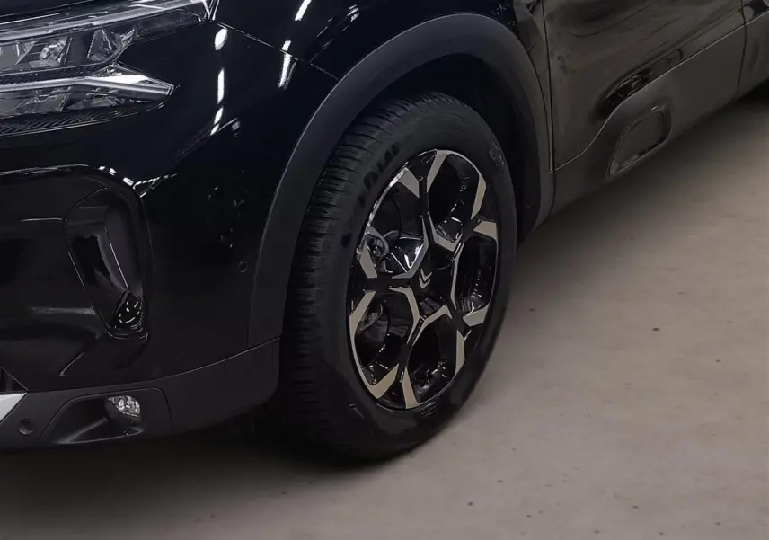 Gros plan sur la roue avant droite et le pare-chocs noir Perla du Citroën C5 Aircross Hybrid 2025.