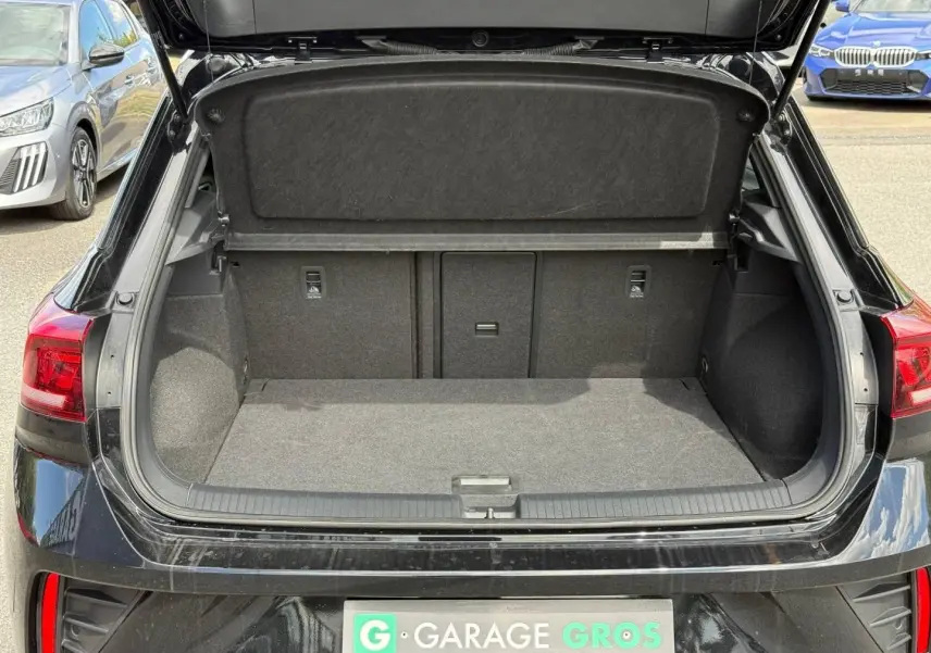 Coffre ouvert vu de l'arrière d'un Volkswagen T-Roc noir intense nacré, avec intérieur de coffre gris et banquette rabattable.