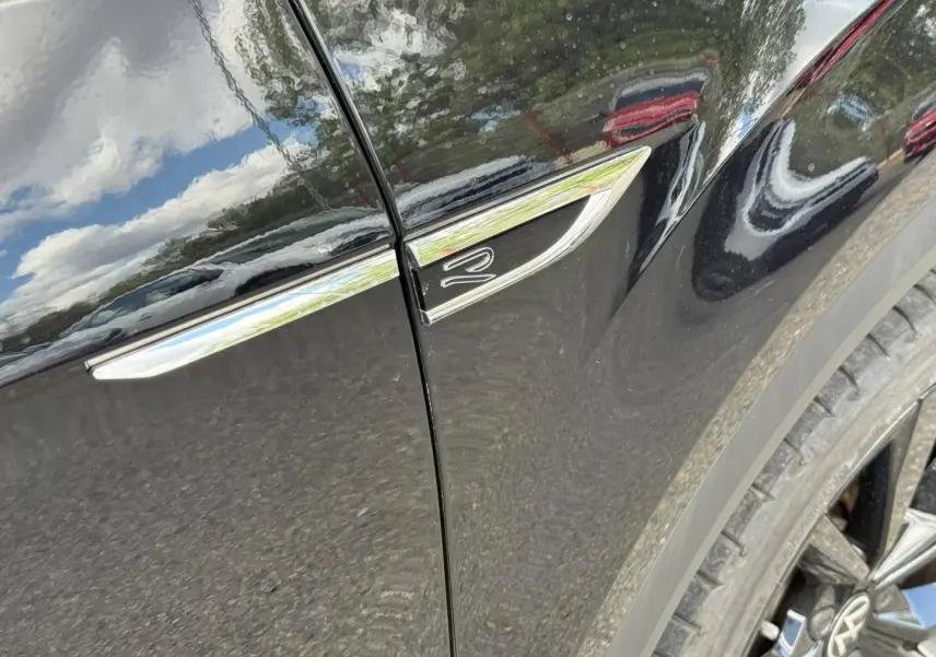 Gros plan sur l’aile avant droite noire nacrée du Volkswagen T-Roc avec logo R et jante alu visible.