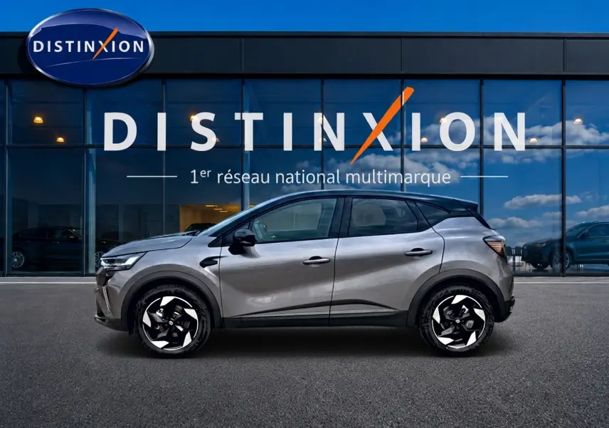 Profil droit d'un Renault Captur 1.8 e-tech hybride 2026 gris Cassiope avec toit noir devant un showroom Distinxion.