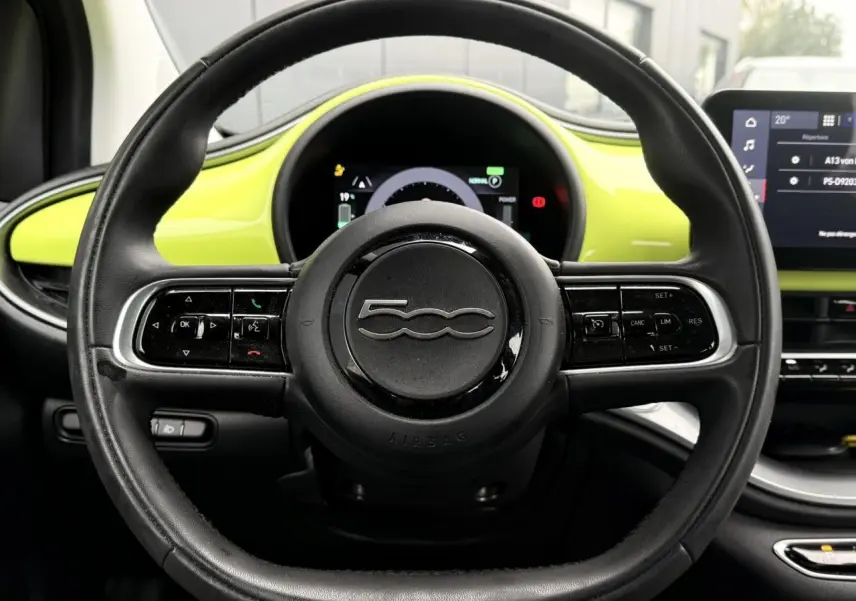 Vue intérieure centrée sur le volant noir de la Fiat 500 électrique 2024 avec tableau de bord jaune Acid en arrière-plan.