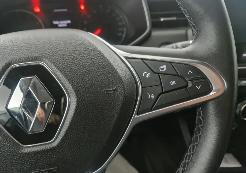 Gros plan sur le volant noir de la Renault Clio V 1.0 TCE 90 Zen, avec commandes multifonctions à droite et logo chromé central.