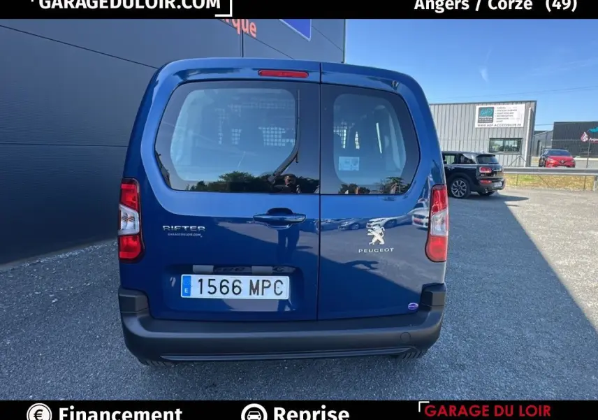 Vue arrière d'un Peugeot Rifter bleu 2024 avec portes battantes et logo visible sur parking extérieur.