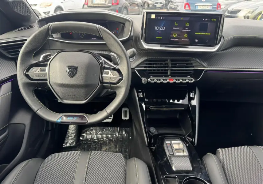 Vue intérieure avant du Peugeot 208 Hybrid 110 e-DCS6 GT gris, volant compact, écran tactile et console centrale moderne.