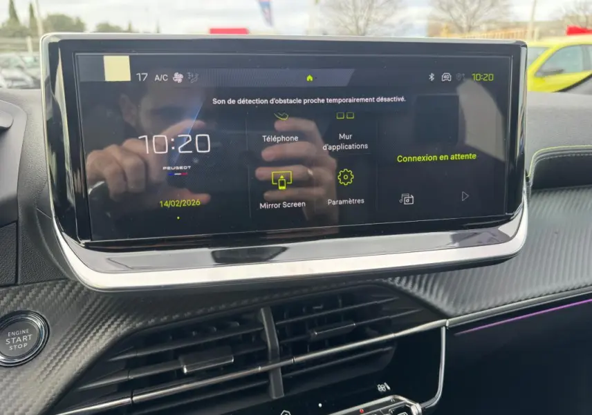 Écran tactile central allumé du tableau de bord de la Peugeot 208 Hybrid 110 gris, avec commandes visibles et finition carbone.