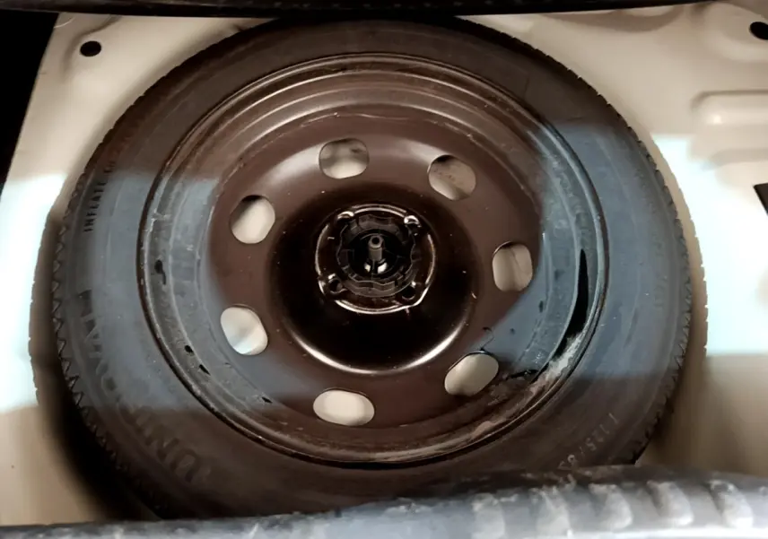 Roue de secours noire montée dans le coffre blanc d'une Citroën C3 BlueHDi 2022, vue de dessus.