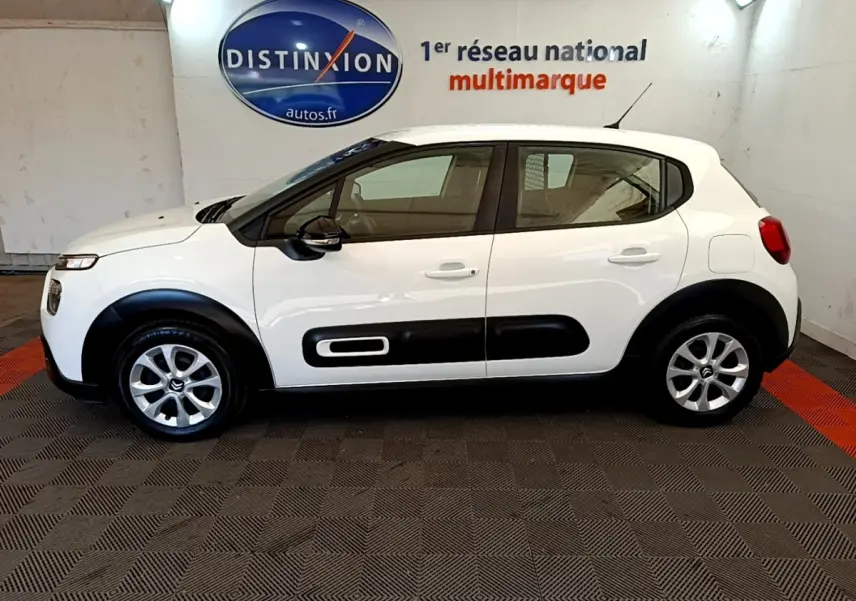 Profil côté gauche d'une Citroën C3 blanche 2022 avec protections latérales noires et jantes alliage en intérieur showroom.