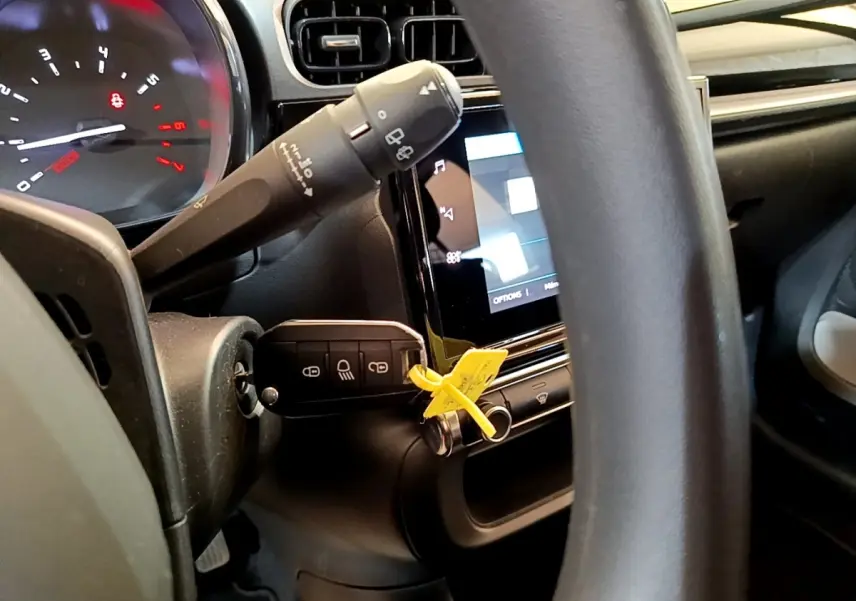 Gros plan sur le volant et le tableau de bord noir de la Citroën C3 blanche, avec la clé insérée et l'écran tactile allumé.