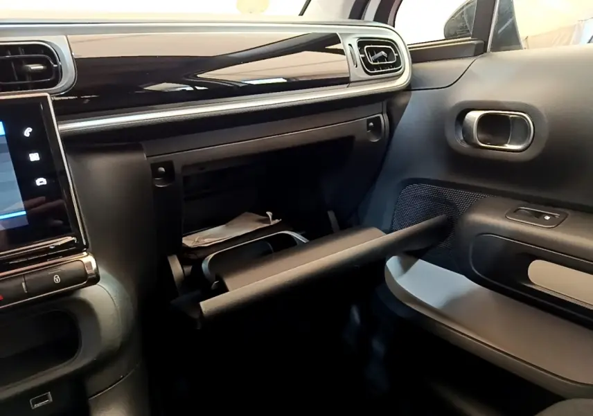 Intérieur de la Citroën C3 blanc, vue côté passager avec boîte à gants ouverte et tableau de bord noir brillant.